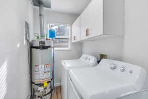 Washroom with cabinets, secured water heater, separate washer and dryer (included), and light hardwood / wood-style flooring