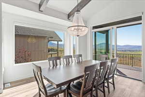 Dining space featuring vaulted ceiling with beams, light hardwood / wood-style flooring, a mountain view, and a notable chandelier