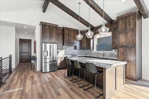 Kitchen featuring decorative backsplash, light hardwood / wood-style flooring, light stone countertops, a center island, and stainless steel fridge with ice dispenser