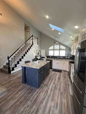 Kitchen featuring white cabinets, hardwood / wood-style floors, ceiling fan, appliances with stainless steel finishes, and vaulted ceiling with skylight