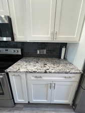 Kitchen featuring white cabinets, backsplash, granite countertops, LVP flooring, and stainless steel appliances