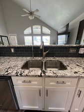 Kitchen featuring lofted ceiling, stainless steel dishwasher, and white cabinets sink faces family room