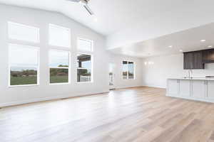 Unfurnished living room with sink, vaulted ceiling, light hardwood / wood-style flooring, and ceiling fan with notable chandelier