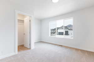 Unfurnished bedroom with a walk in closet, light colored carpet, and a closet