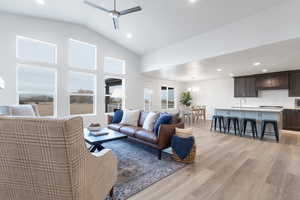 Living room featuring ceiling fan with notable chandelier, light hardwood / wood-style floors, vaulted ceiling, and sink