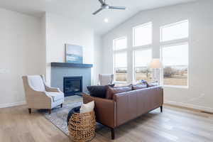 Living room featuring a fireplace, light wood-type flooring, ceiling fan, and lofted ceiling