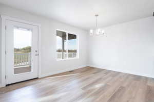 Unfurnished dining area with light hardwood / wood-style flooring, a textured ceiling, and an inviting chandelier