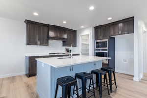 Kitchen featuring sink, stainless steel appliances, tasteful backsplash, light hardwood / wood-style floors, and a kitchen island with sink