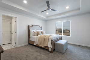 Carpeted bedroom featuring a raised ceiling and ceiling fan