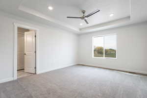 Carpeted empty room featuring ceiling fan, a textured ceiling, and a tray ceiling