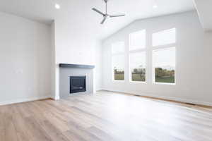 Unfurnished living room featuring vaulted ceiling, a tiled fireplace, light wood-type flooring, and ceiling fan