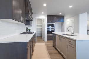 Kitchen with sink, stainless steel appliances, premium range hood, an island with sink, and light wood-type flooring