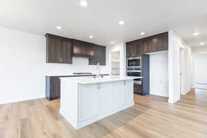 Kitchen featuring dark brown cabinets, appliances with stainless steel finishes, a kitchen island with sink, light hardwood / wood-style floors, and sink