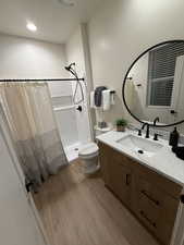 Bathroom with hardwood / wood-style floors, vanity, toilet, and curtained shower