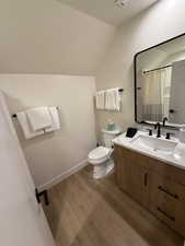 Bathroom with curtained shower, lofted ceiling, toilet, vanity, and hardwood / wood-style flooring