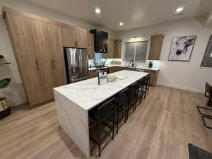 Kitchen featuring a center island, sink, a kitchen breakfast bar, stainless steel fridge with ice dispenser, and light hardwood / wood-style floors