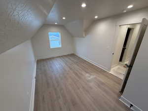 Additional living space with light hardwood / wood-style floors, a textured ceiling, and vaulted ceiling