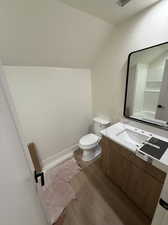 Bathroom with vanity, hardwood / wood-style floors, vaulted ceiling, and toilet