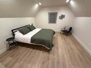 Bedroom featuring a textured ceiling, light hardwood / wood-style flooring, and lofted ceiling