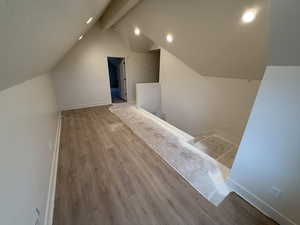 Additional living space with vaulted ceiling with beams and light wood-type flooring