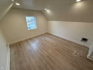 Additional living space with lofted ceiling, a textured ceiling, and wood-type flooring