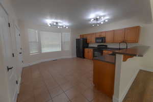 Kitchen with a breakfast bar area, kitchen peninsula, black appliances, a notable chandelier, and light tile patterned floors