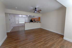 Unfurnished living room featuring dark hardwood / wood-style floors and ceiling fan with notable chandelier