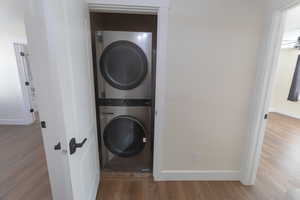 Laundry area featuring stacked washer / drying machine and wood-type flooring