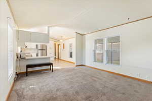 Unfurnished living room with a notable chandelier, ornamental molding, and light colored carpet