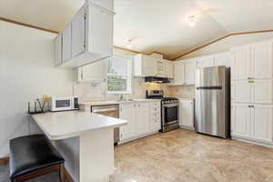 Kitchen with vaulted ceiling, appliances with stainless steel finishes, kitchen peninsula, and white cabinetry