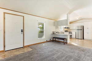 Kitchen featuring a kitchen bar, kitchen peninsula, stainless steel appliances, vaulted ceiling, and white cabinets