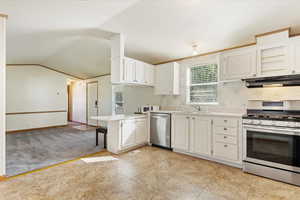 Kitchen featuring kitchen peninsula, white cabinets, vaulted ceiling, sink, and stainless steel appliances