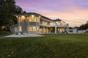 Back house at dusk with a garage, an outdoor structure, a balcony, a lawn, and a patio area