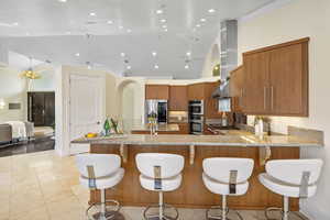 Kitchen featuring island range hood, appliances with stainless steel finishes, a kitchen bar, and kitchen peninsula