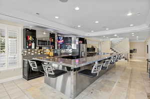 Kitchen featuring decorative backsplash, a spacious island, a breakfast bar, dark stone countertops, and stainless steel appliances