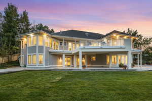 Back house at dusk with a balcony, a patio, and a lawn