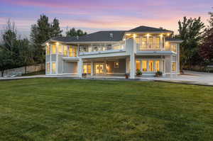 Back house at dusk with a patio, french doors, a yard, and a balcony