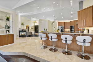 Kitchen with appliances with stainless steel finishes, a multi sided fireplace, high vaulted ceiling, and a kitchen breakfast bar