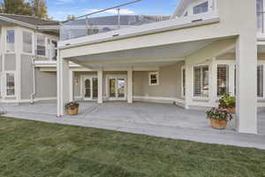 Back of property featuring a balcony, a patio area, and a lawn