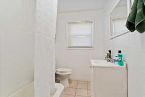 Full bathroom with tile patterned floors, plus walk in shower, toilet, vanity, and tile walls