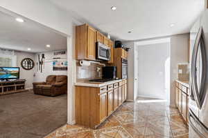 Kitchen with appliances with stainless steel finishes, light colored carpet, tile counters, and tasteful backsplash