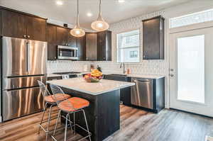 Kitchen featuring pendant lighting, a kitchen island, appliances with stainless steel finishes, and dark brown cabinets