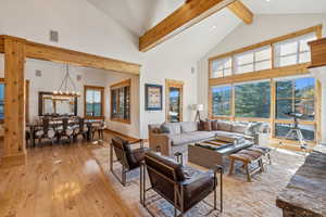 Living room featuring high vaulted ceiling, beamed ceiling, an inviting chandelier, and light wood-type flooring