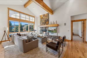 Living room featuring light hardwood / wood-style floors, a stone fireplace, high vaulted ceiling, and beamed ceiling