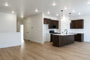 Kitchen with a center island with sink, decorative light fixtures, light hardwood / wood-style floors, and appliances with stainless steel finishes