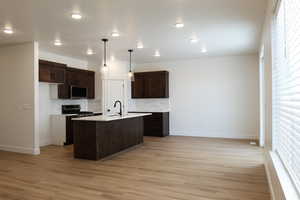 Kitchen featuring hanging light fixtures, tasteful backsplash, light hardwood / wood-style floors, a kitchen island with sink, and appliances with stainless steel finishes