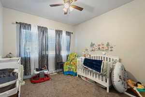 Carpeted bedroom featuring ceiling fan and a crib