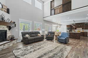 Living room with a stone fireplace, a towering ceiling, a chandelier, and light wood-type flooring