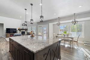 Kitchen featuring a kitchen island, a fireplace, hanging light fixtures, light stone counters, and hardwood / wood-style flooring