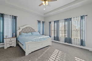 Carpeted bedroom featuring ceiling fan and a raised ceiling